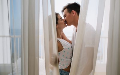 graceful girl white tank top gently kissing her brunette boyfriend hiding light curtains portait romantic young couple spending time together balcony enjoying each other