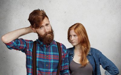 confused bearded man feeling guilty scratching his head confusion while his redhead girlfriend wife standing him looking with angry disappointed expression holding hands her waist