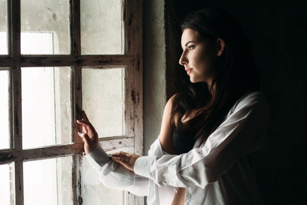 Mulher pensativa olhando pela janela representando relacionamento abusivo, conflito emocional e sensação de prisão psicológica